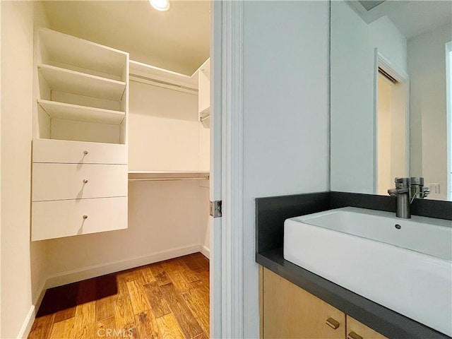 bathroom with baseboards, wood finished floors, a walk in closet, vanity, and recessed lighting