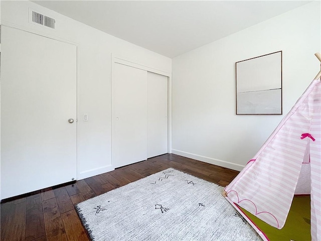 unfurnished bedroom with dark wood-style floors, a closet, visible vents, and baseboards