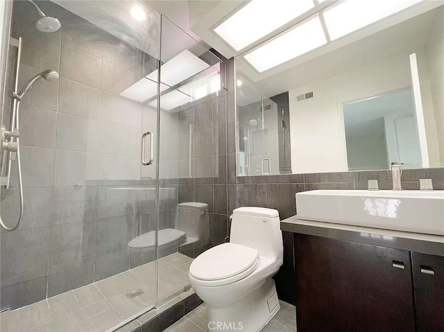 bathroom featuring tile walls, visible vents, toilet, a stall shower, and vanity