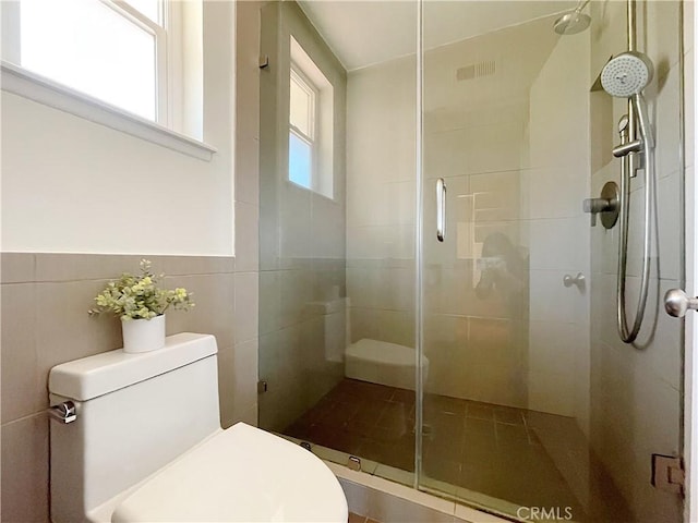 bathroom featuring toilet, a stall shower, and tile walls