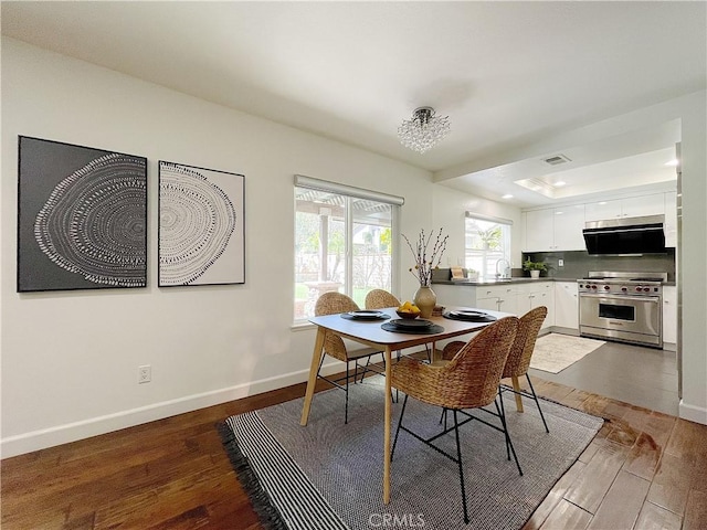 dining space featuring a tray ceiling, wood finished floors, visible vents, and baseboards