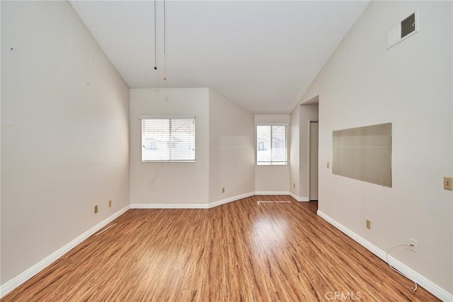 unfurnished room featuring light wood-style floors, lofted ceiling, visible vents, and baseboards