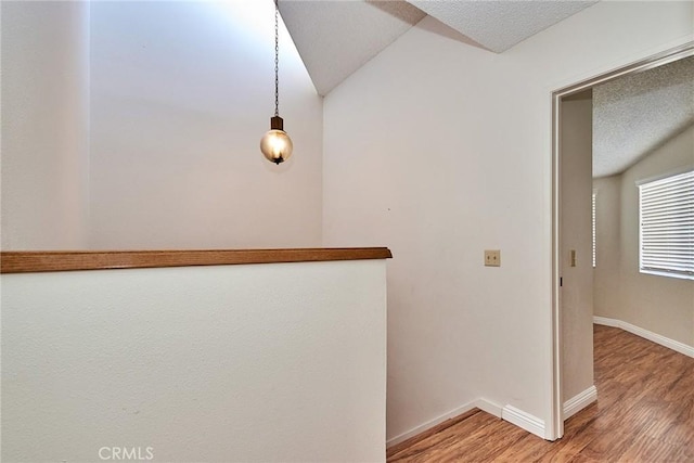 hall with a textured ceiling, light wood finished floors, lofted ceiling, and baseboards