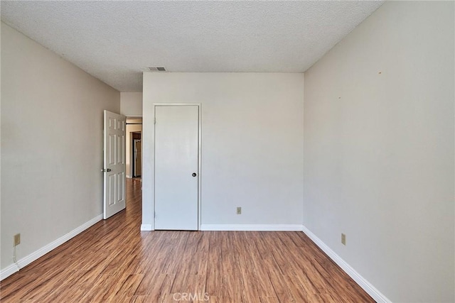 spare room featuring visible vents, a textured ceiling, baseboards, and wood finished floors