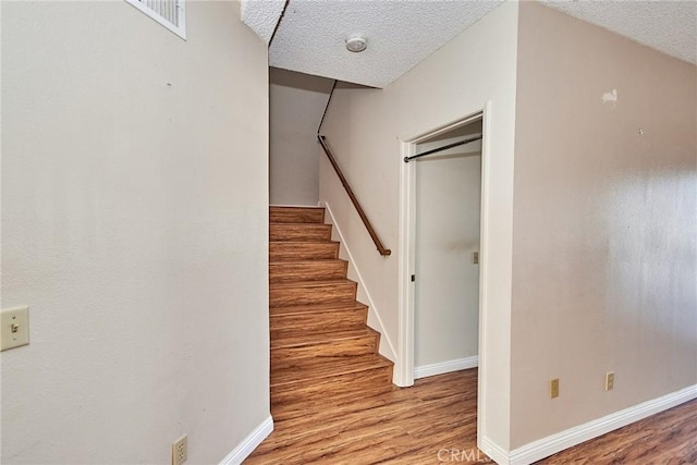 staircase featuring a textured ceiling, baseboards, and wood finished floors