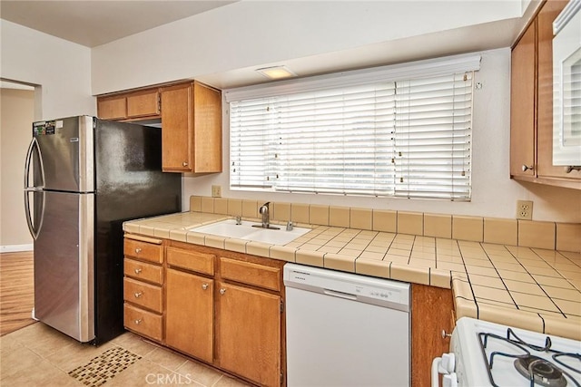 kitchen featuring light tile patterned floors, white appliances, brown cabinetry, and a sink