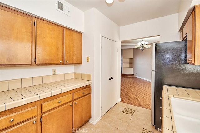 kitchen with brown cabinetry, freestanding refrigerator, visible vents, and light tile patterned floors