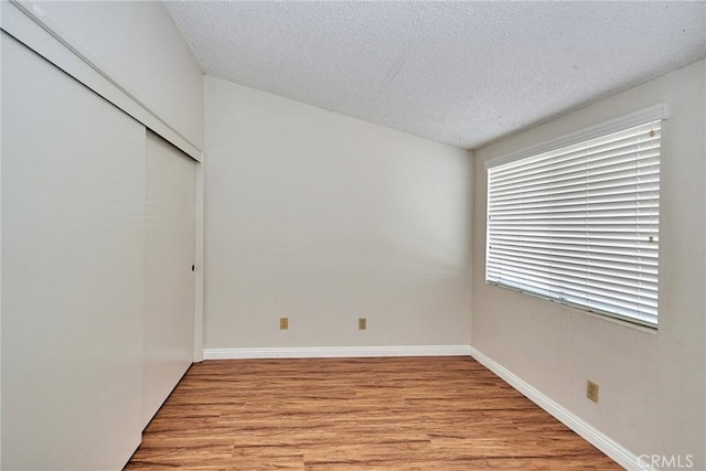 unfurnished bedroom with a textured ceiling, a closet, baseboards, and light wood-style floors