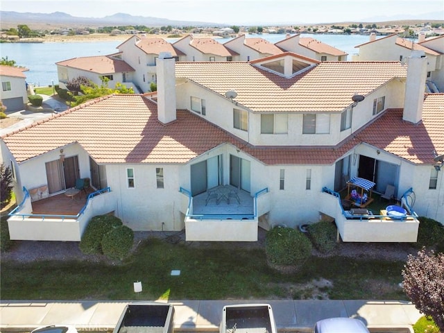 back of house with a water view, a tile roof, a residential view, and stucco siding