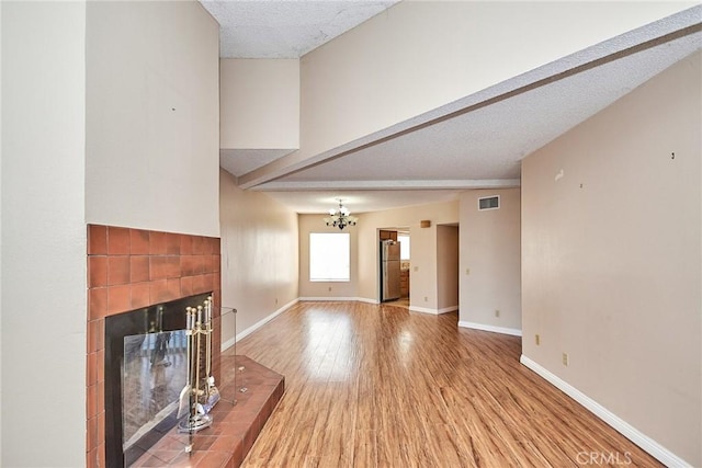 unfurnished living room featuring baseboards, visible vents, a tiled fireplace, and wood finished floors