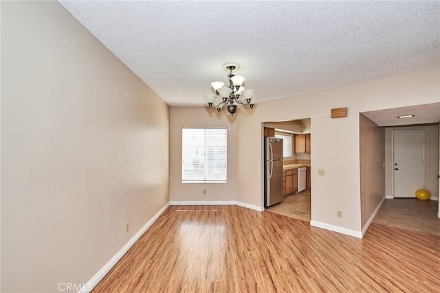 empty room featuring light wood-type flooring, a textured ceiling, baseboards, and an inviting chandelier