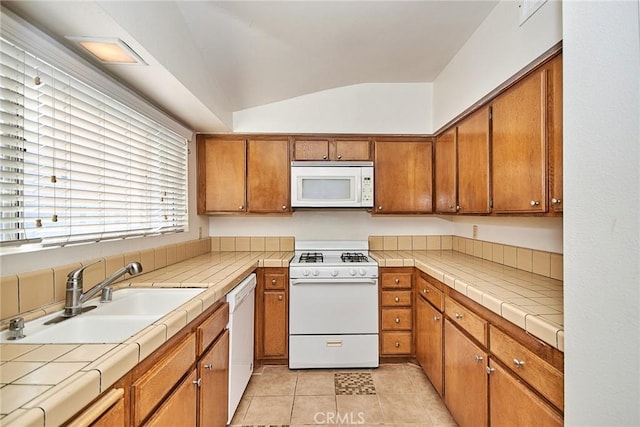 kitchen with white appliances, tile countertops, lofted ceiling, brown cabinets, and a sink