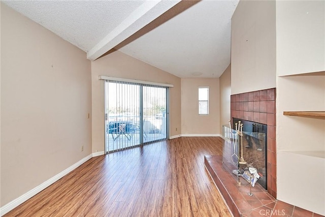 unfurnished living room with vaulted ceiling with beams, a textured ceiling, a tile fireplace, wood finished floors, and baseboards