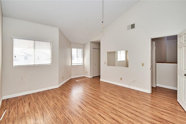 unfurnished bedroom with light wood finished floors, baseboards, visible vents, and high vaulted ceiling