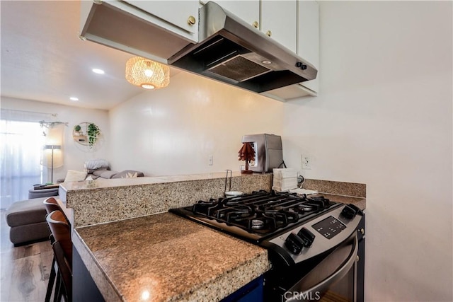 kitchen featuring open floor plan, wood finished floors, under cabinet range hood, a peninsula, and stainless steel gas range oven