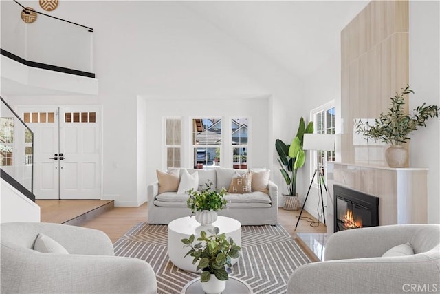 living area featuring high vaulted ceiling, light wood-type flooring, baseboards, and a premium fireplace