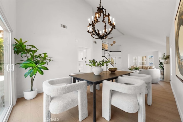 dining space featuring light wood finished floors, baseboards, visible vents, and high vaulted ceiling