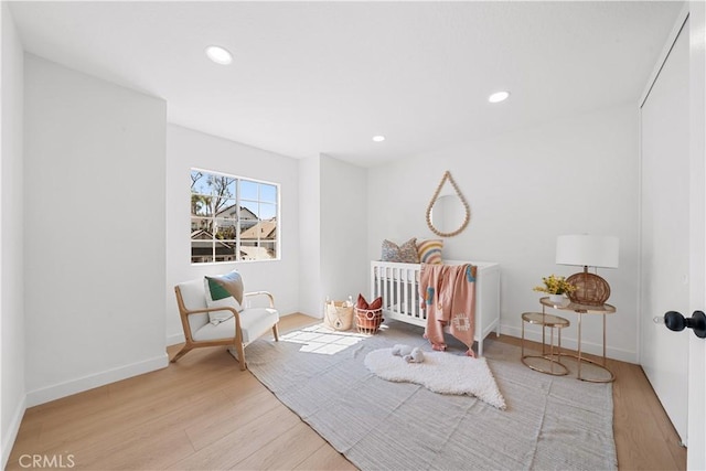 bedroom with recessed lighting, baseboards, a nursery area, and wood finished floors