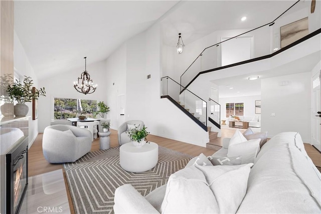 living room featuring high vaulted ceiling, a notable chandelier, a lit fireplace, and stairs