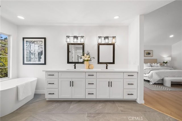 full bathroom with double vanity, a freestanding tub, connected bathroom, and a sink