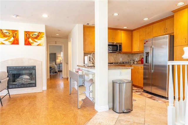 kitchen featuring recessed lighting, light countertops, appliances with stainless steel finishes, decorative backsplash, and a glass covered fireplace