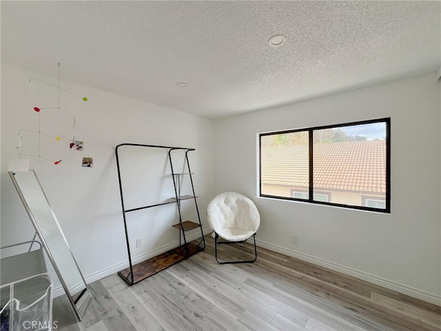 unfurnished room with light wood-type flooring, a textured ceiling, and baseboards