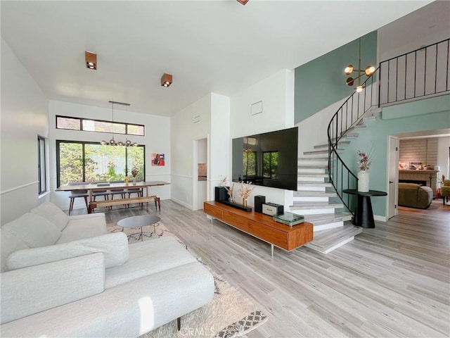 living room featuring baseboards, a towering ceiling, wood finished floors, stairs, and a notable chandelier