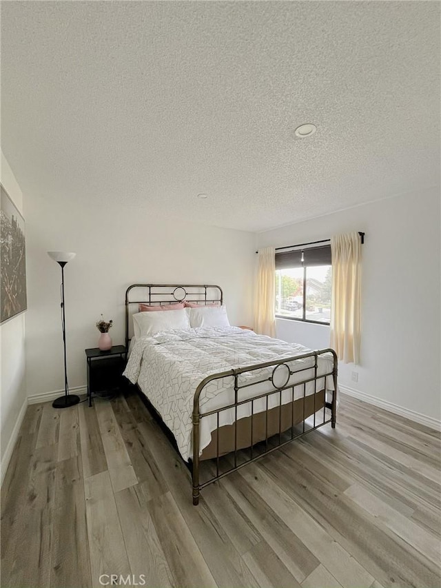 bedroom with baseboards, a textured ceiling, and light wood-style floors