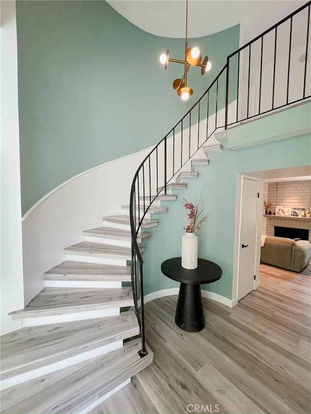 staircase featuring a chandelier, baseboards, a high ceiling, and wood finished floors