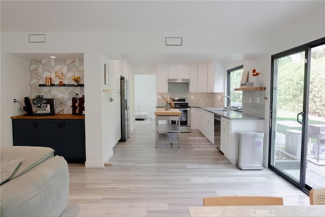 kitchen featuring white cabinets, appliances with stainless steel finishes, backsplash, light wood-type flooring, and a sink