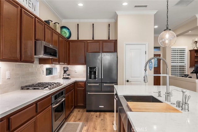 kitchen featuring appliances with stainless steel finishes, decorative light fixtures, crown molding, light wood-type flooring, and backsplash