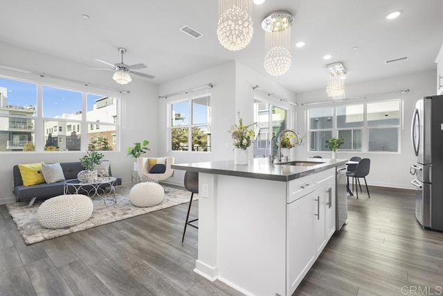 kitchen featuring a center island with sink, visible vents, dark wood-style floors, stainless steel appliances, and a sink