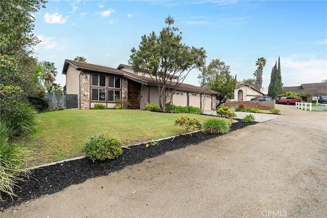 view of front of property with driveway, stone siding, fence, a front yard, and a garage