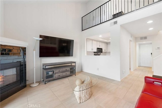 living room with a tile fireplace, visible vents, a high ceiling, and recessed lighting