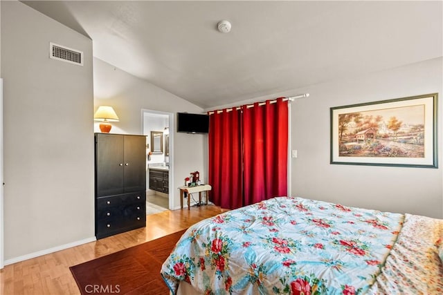 bedroom featuring light wood finished floors, visible vents, vaulted ceiling, ensuite bath, and baseboards