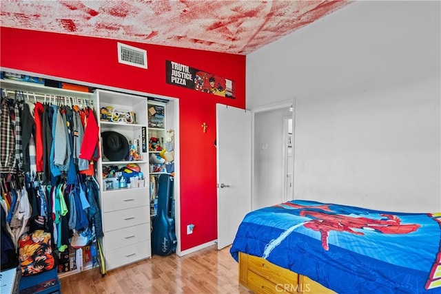 bedroom with a closet, visible vents, vaulted ceiling, and wood finished floors