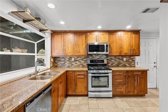 kitchen with visible vents, brown cabinetry, light stone countertops, stainless steel appliances, and a sink