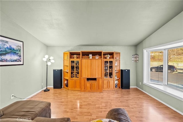 living area with vaulted ceiling, baseboards, and wood finished floors