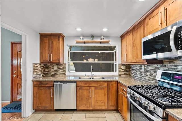 kitchen featuring stainless steel appliances, brown cabinetry, a sink, and light stone countertops