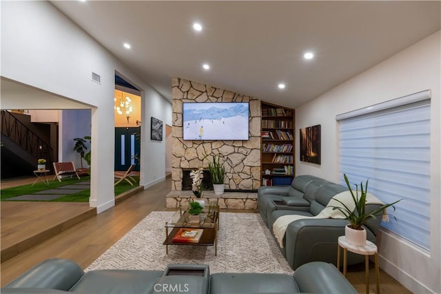 living area with lofted ceiling, a stone fireplace, recessed lighting, wood finished floors, and built in features