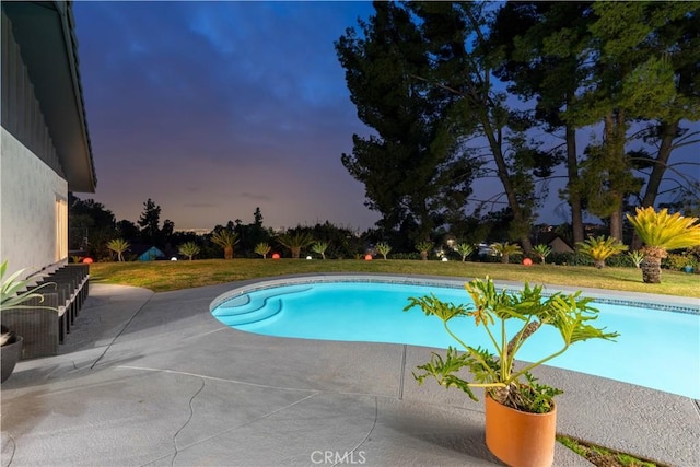 pool at dusk with a yard, a patio area, and an outdoor pool