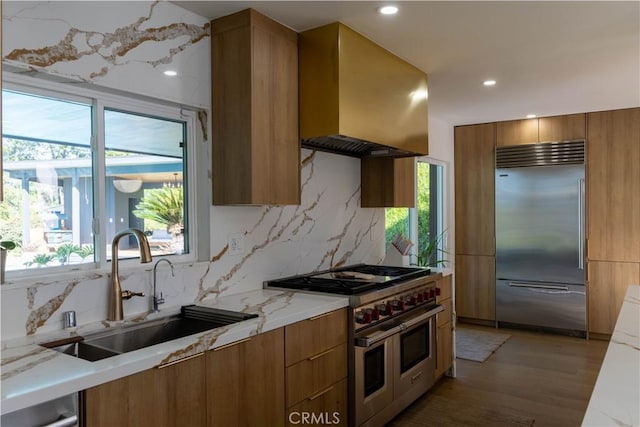 kitchen with brown cabinetry, premium appliances, modern cabinets, wall chimney range hood, and a sink