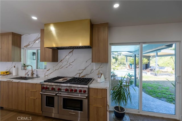 kitchen featuring modern cabinets, light countertops, wall chimney range hood, double oven range, and a sink