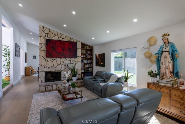 living room with lofted ceiling, a stone fireplace, wood finished floors, and recessed lighting