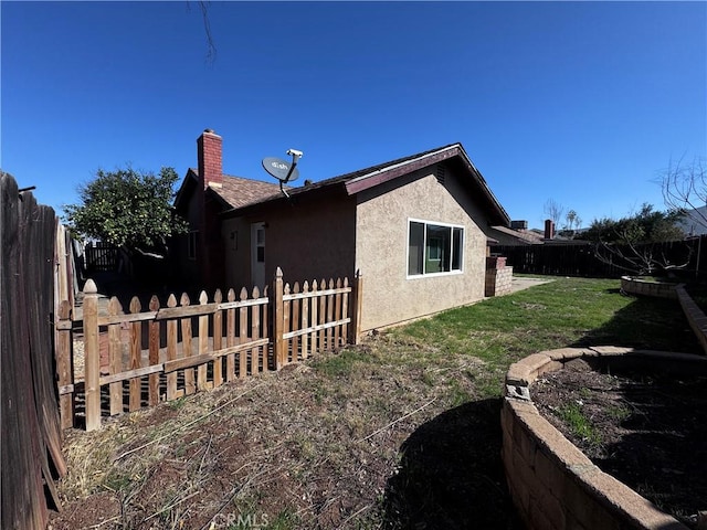 view of property exterior featuring a chimney, a fenced backyard, a lawn, and stucco siding