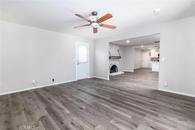 unfurnished living room featuring a brick fireplace, baseboards, dark wood-style floors, and ceiling fan