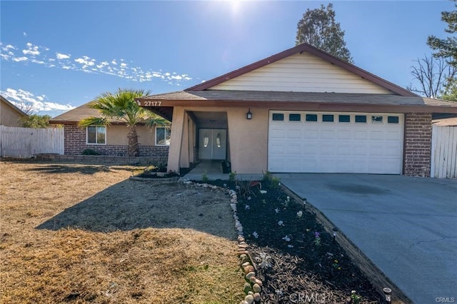 single story home with driveway, brick siding, an attached garage, fence, and stucco siding