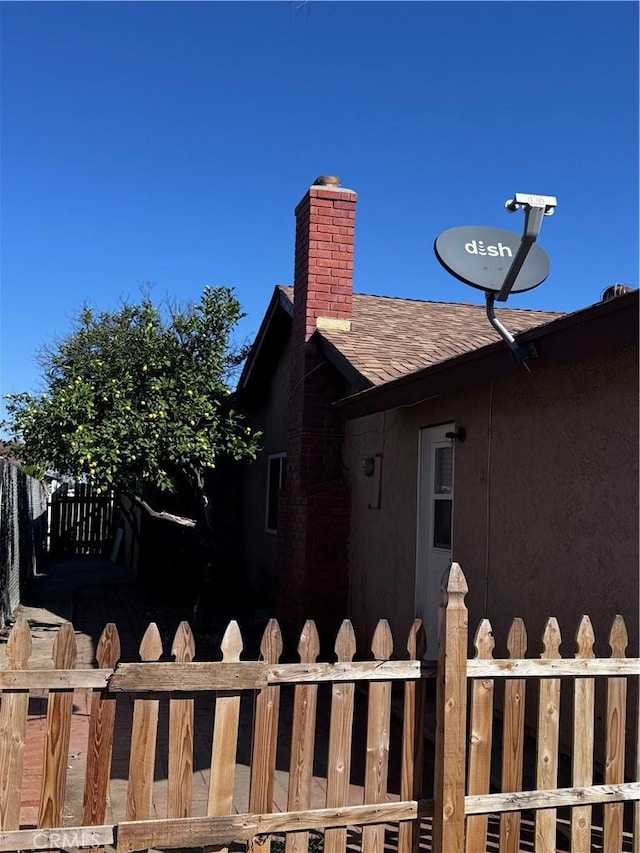 view of property exterior with roof with shingles, fence, and a chimney