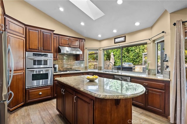 kitchen featuring a kitchen island, light stone counters, stainless steel appliances, under cabinet range hood, and a sink