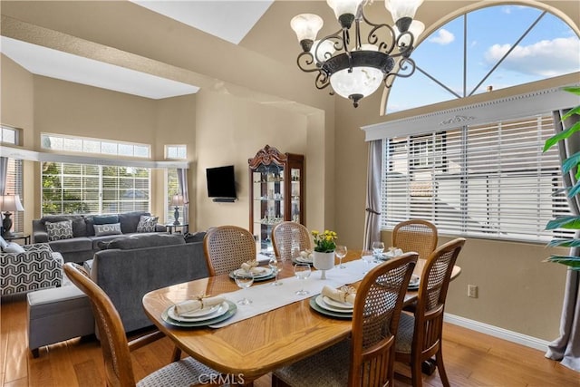 dining area with a chandelier, a high ceiling, baseboards, and wood finished floors